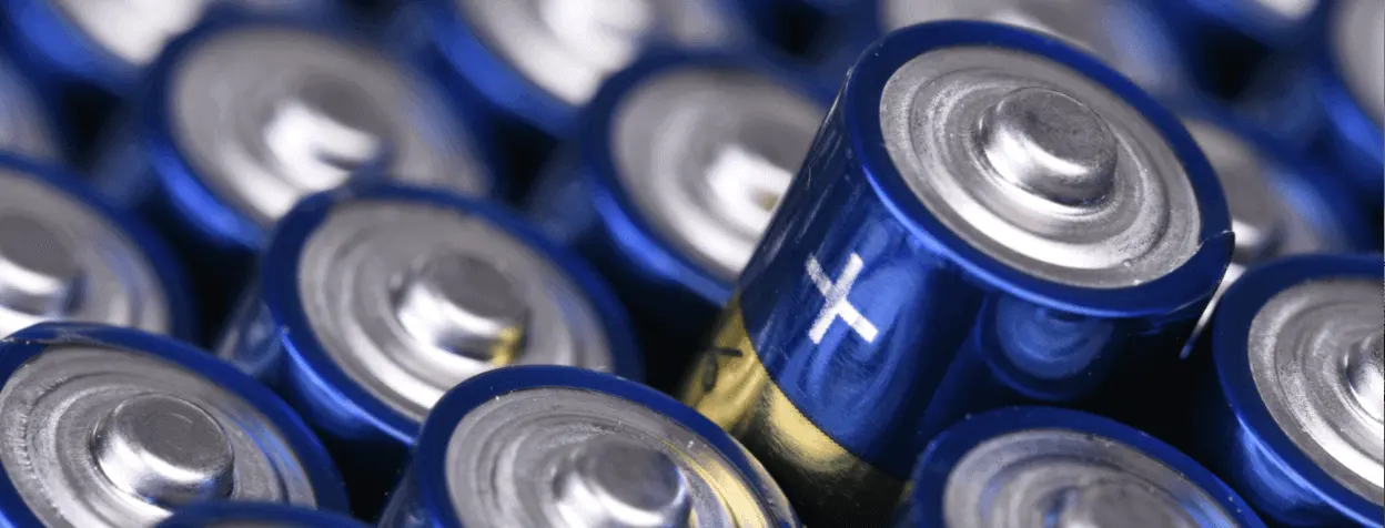 A close-up view of several blue AA batteries tightly packed together, with the metallic positive terminal and plus sign indicating the positive end. East-West Electric, renowned Tampa Bay electrical contractors, ensure precision in details like the one uniquely angled battery in this focused shot.