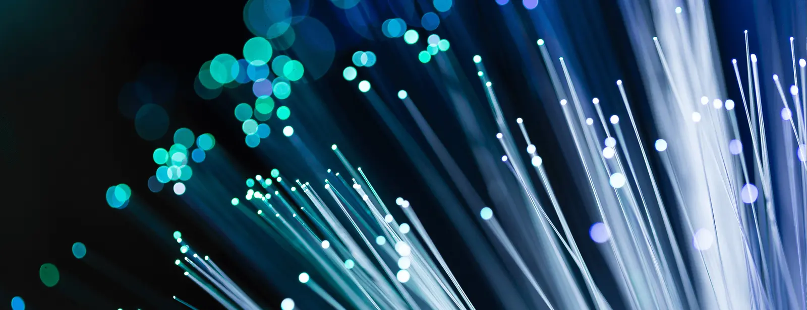 A close-up of optical fiber cables illuminated with blue and green light against a dark background. The image shows numerous thin, glowing strands spreading outwards, creating a dynamic and vibrant effect with bright bokeh lights in the background, capturing the precision associated with Tampa Bay electrical contractors.