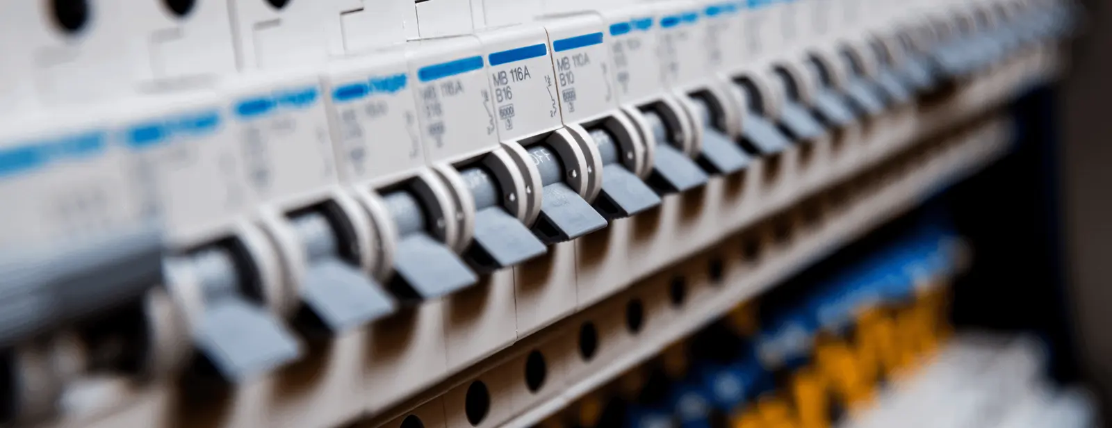 Close-up of a row of electrical circuit breakers with switches in an electrical panel. The breakers are aligned in an orderly fashion, each labeled with specifications, and the panel is part of the electrical distribution system installed by East-West Electric, your commercial electrician near me.